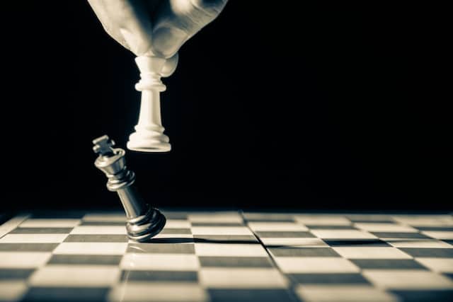 white chess piece knocking over black chess piece